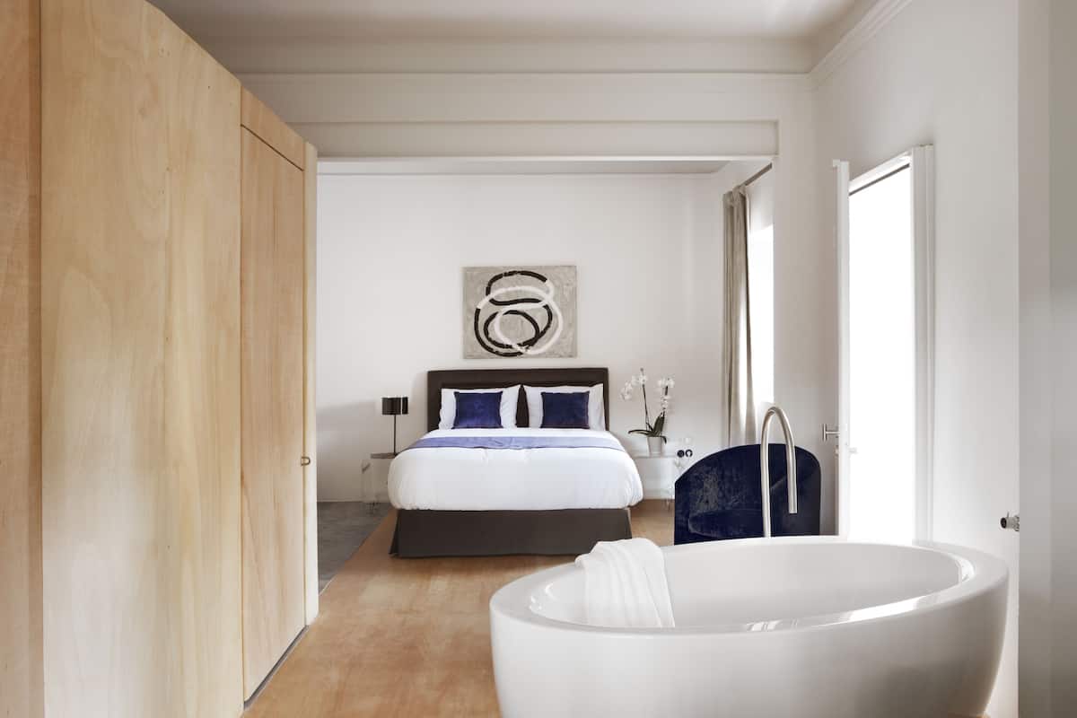 A modern bedroom with a large bed, a bathtub, and a wooden wardrobe.