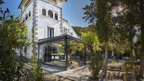 Un bâtiment moderne doté d’une façade en verre et en pierre, ainsi que d’un espace extérieur aménagé pour s’asseoir.