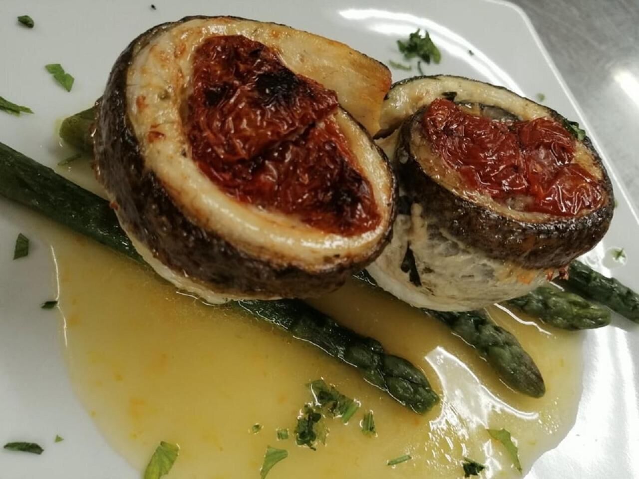 Un plato con un rollito de carne relleno, espárragos y salsa amarilla.