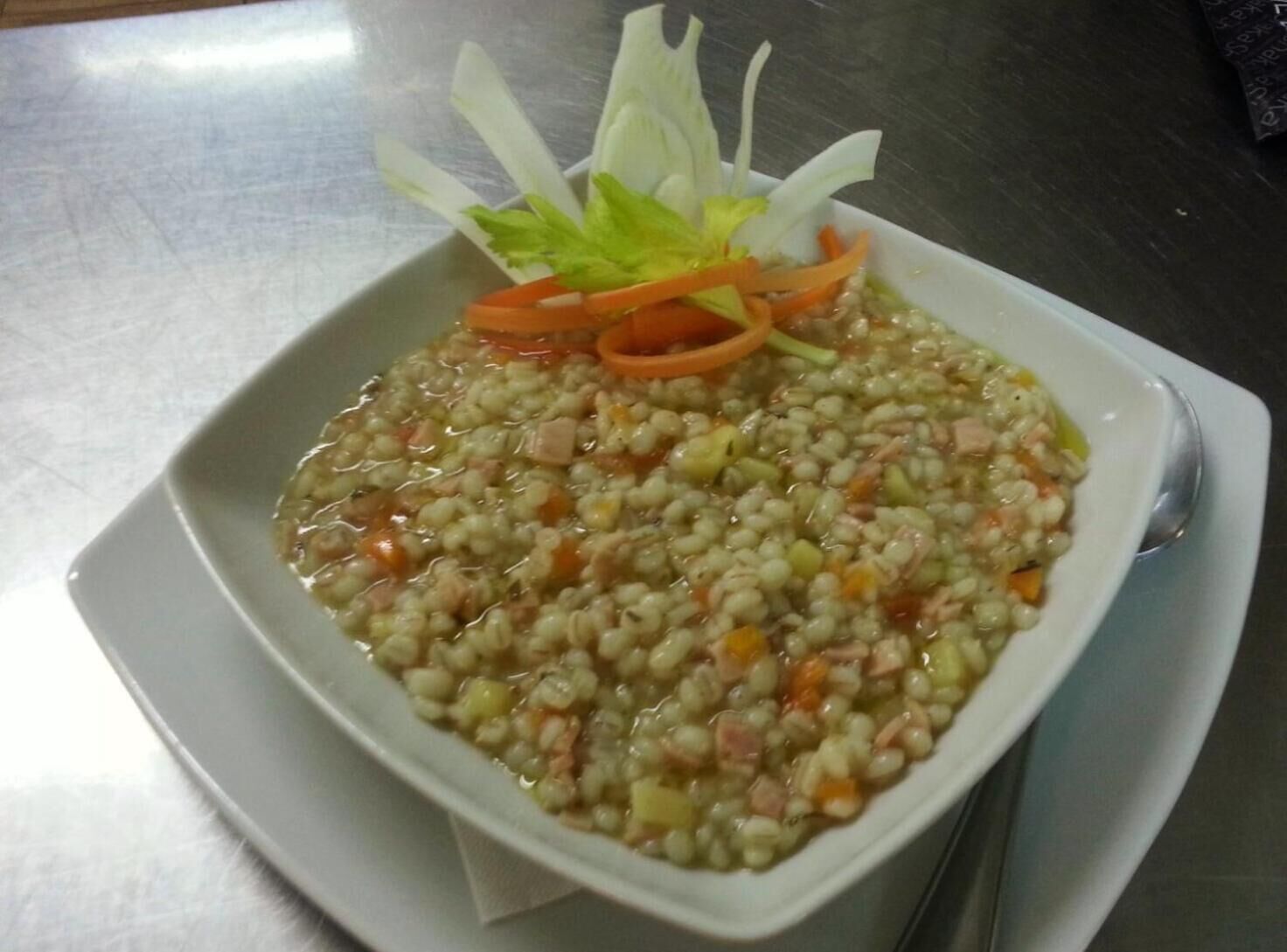 Una ciotola di zuppa di lenticchie con verdure e un condimento di lattuga e fettine di carota su un piatto bianco.
