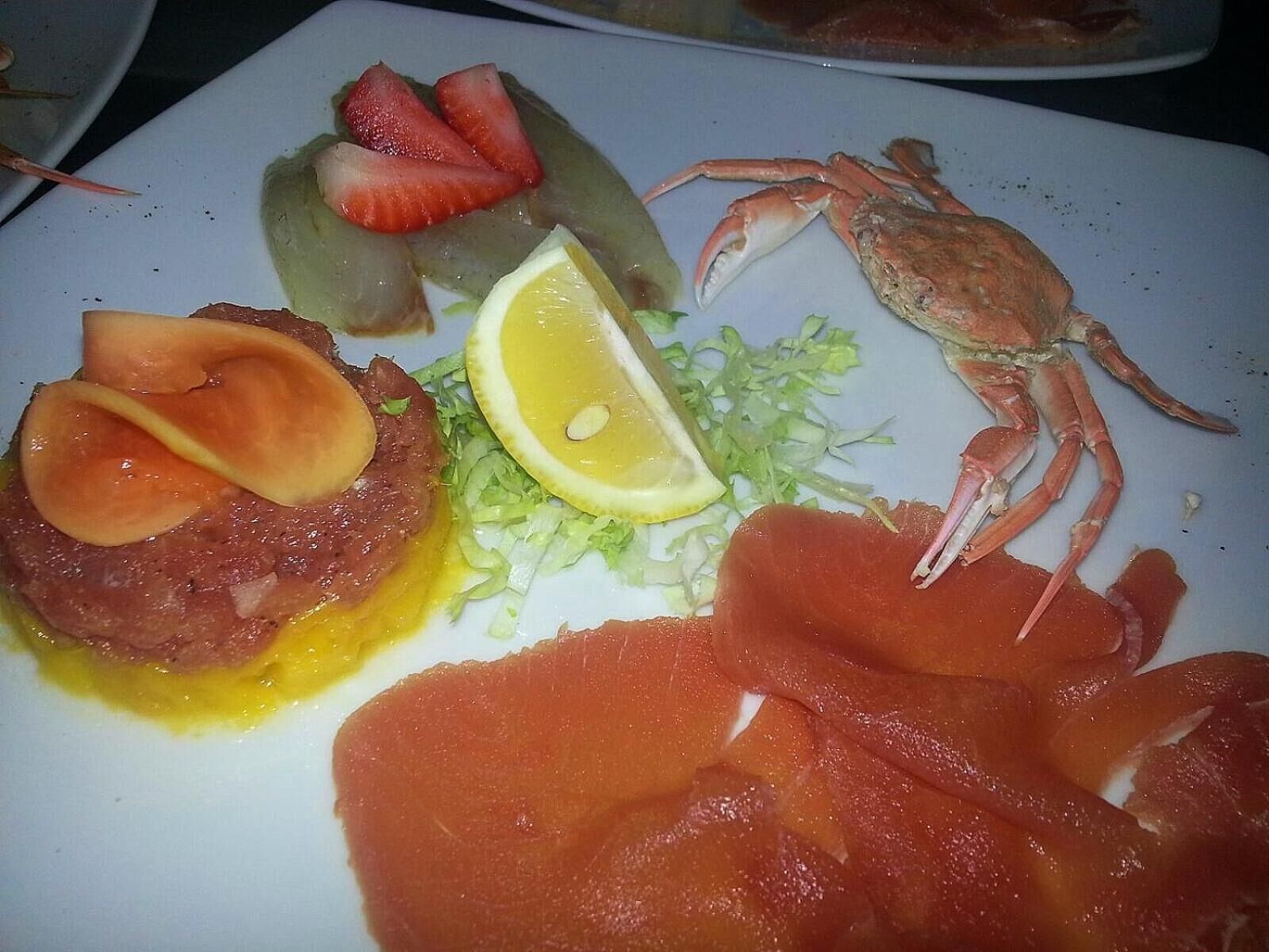 Un piatto con diversi tipi di pesce, tra cui granchio, salmone e un pezzo di carne, accompagnato da una fetta di limone.
