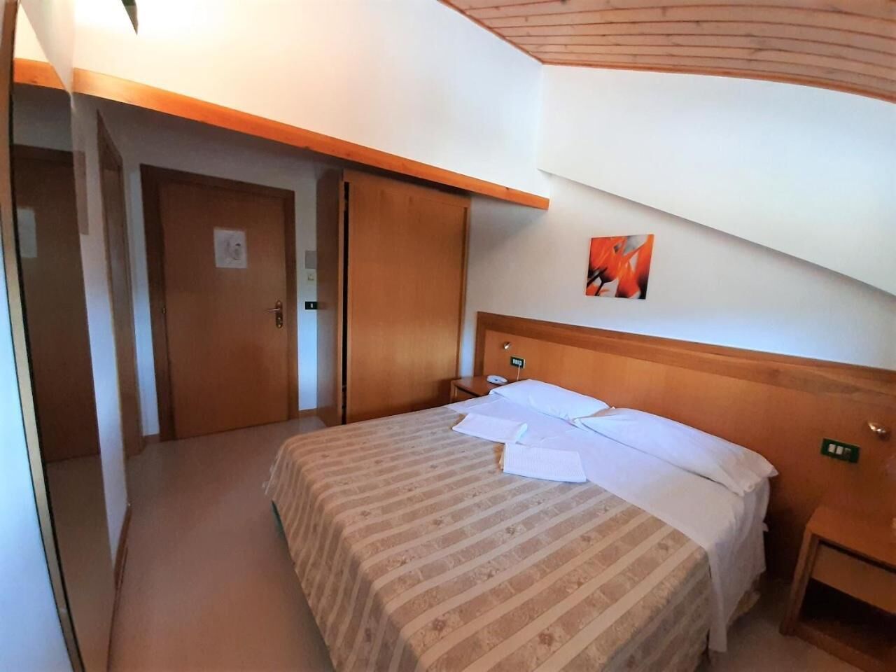 Una camera d'albergo con un letto, una testiera in legno, un comodino e una porta.