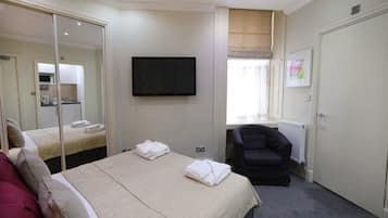 A hotel room with a bed, a TV, a chair, and a bathroom visible through a door.