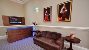 A hotel lobby with a reception desk, a brown leather sofa, a small round table with a decorative item, and two framed paintings on the wall. - Palmerston Suites (Edinburgh)