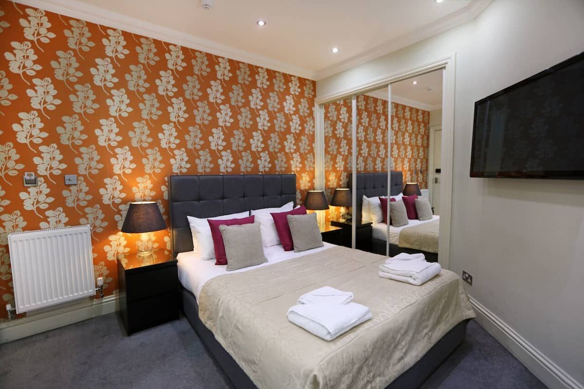 A bedroom with a large bed, a nightstand, a mirror, and a TV.