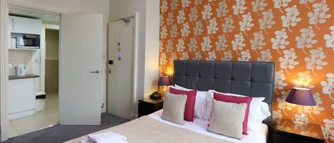 Una habitación de hotel con una cama grande, una mesita de noche con lámpara y un baño visible a través de una puerta abierta.