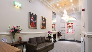 A lobby with a sofa, a wooden table, a vase of flowers, and framed artwork on the wall. - Palmerston Suites (Edinburgh)