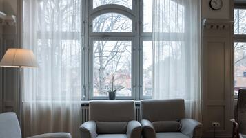 Quarto com duas poltronas, uma mesa e uma janela com cortinas leves.