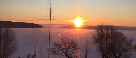 A sunset over a frozen lake with bare trees and a wooden fence in the foreground.