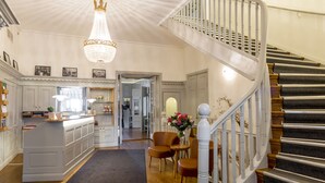 A spacious kitchen with a central island, a chandelier, and a staircase with a wooden railing. - Sigtuna Stadshotell (Sigtuna)