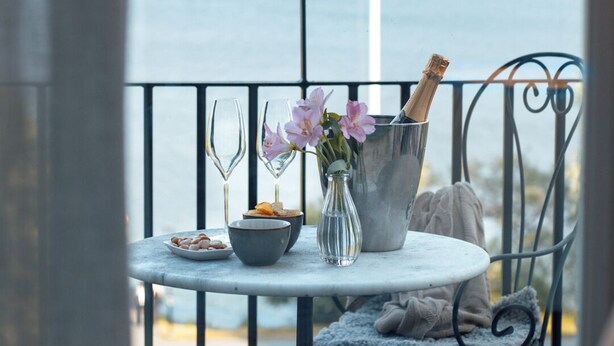 A balcony with a table set for a meal, a vase with flowers, and a bottle of champagne. - Sigtuna Stadshotell (Sigtuna)