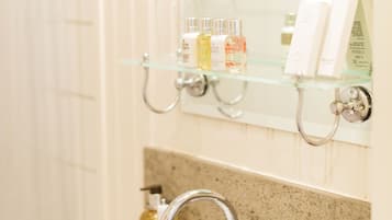 Een badkamer met een wit wastafelmeubel, een glazen plank met toiletartikelen, en een spiegel erboven.
