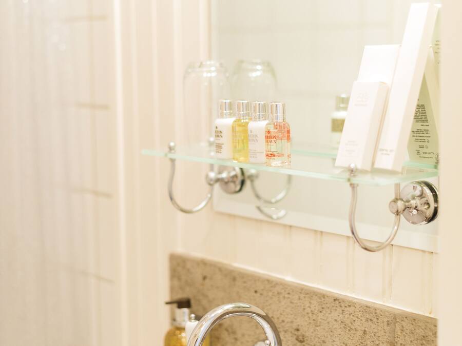 Un baño con lavamanos blanco, un estante de vidrio con artículos de aseo y un espejo sobre el estante.