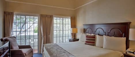 A hotel room with a large bed, a dresser, a chair, a nightstand with a lamp, and a chandelier.