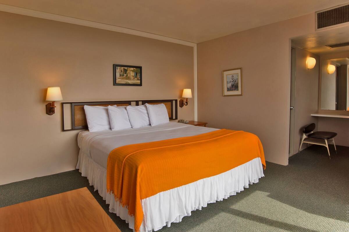 A hotel room with a bed, two wall-mounted lamps, a chair, and a desk.