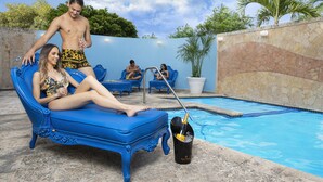 A poolside area with a blue ornate lounge chair, a bucket with a bottle, and a pool. - Meliá Century Hotel Ponce (Ponce)