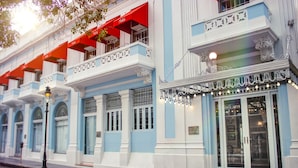 A building with blue and white exterior walls, a balcony with red awnings, and a storefront with glass doors and decorative lighting. - Meliá Century Hotel Ponce (Ponce)