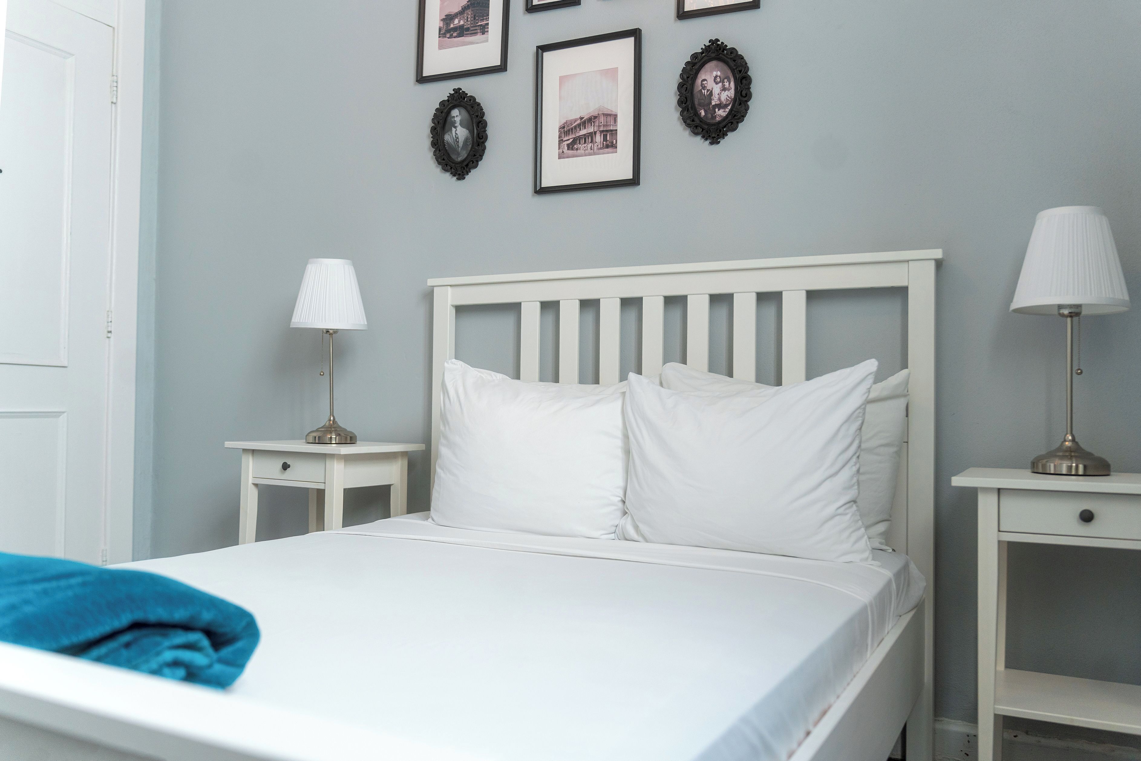 A neatly made bed with white bedding, two bedside tables with lamps, and framed pictures on the wall.