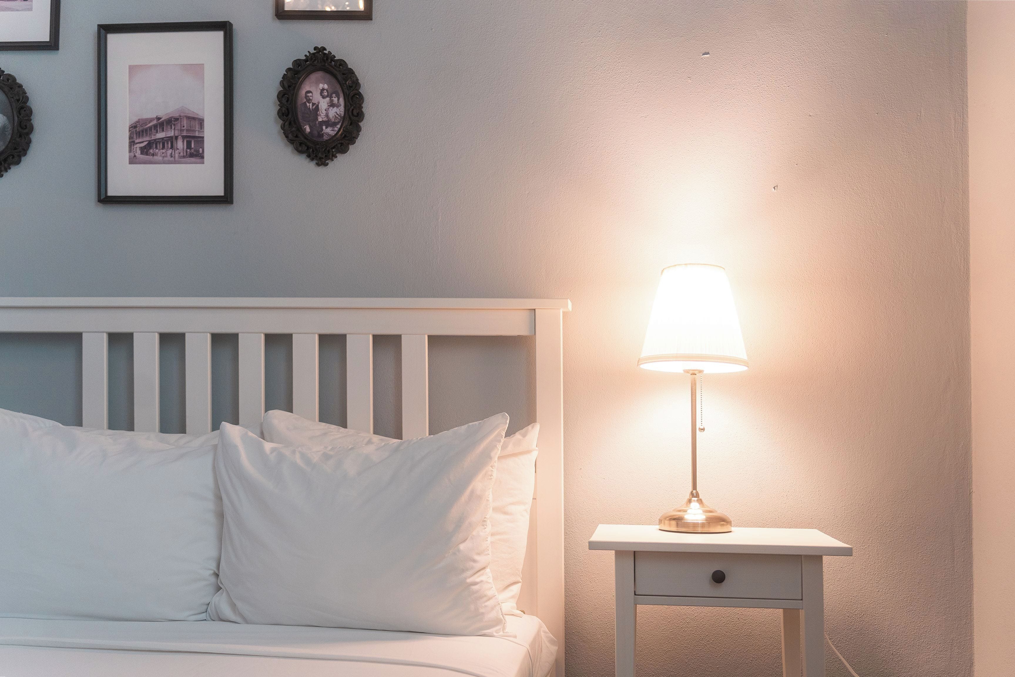 A bedroom with a white bed, a bedside table with a lamp, and framed pictures on the wall.