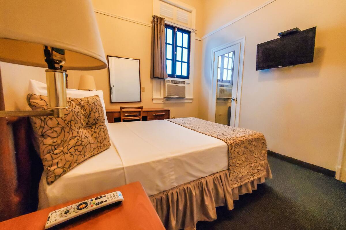 A hotel room with a bed, a desk, a chair, a lamp, a TV, and a window.