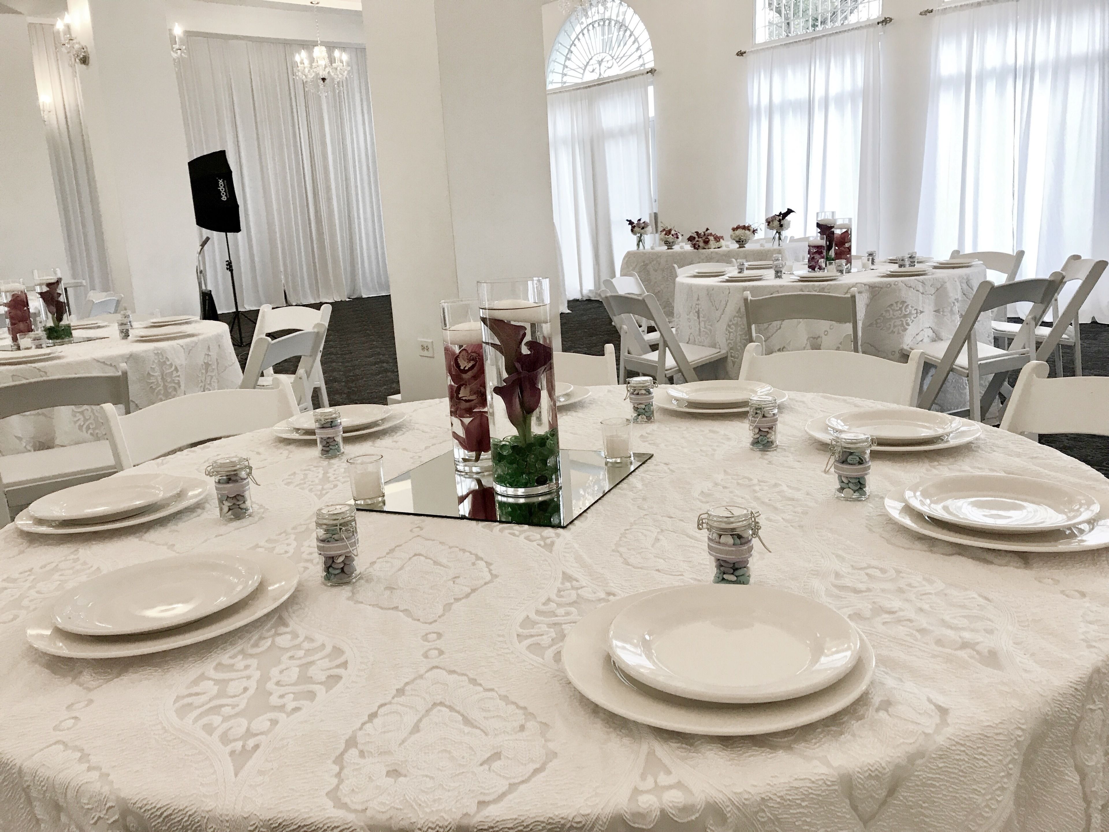 Un comedor con mesas redondas dispuestas para una comida, con manteles blancos y candelabros de vidrio.