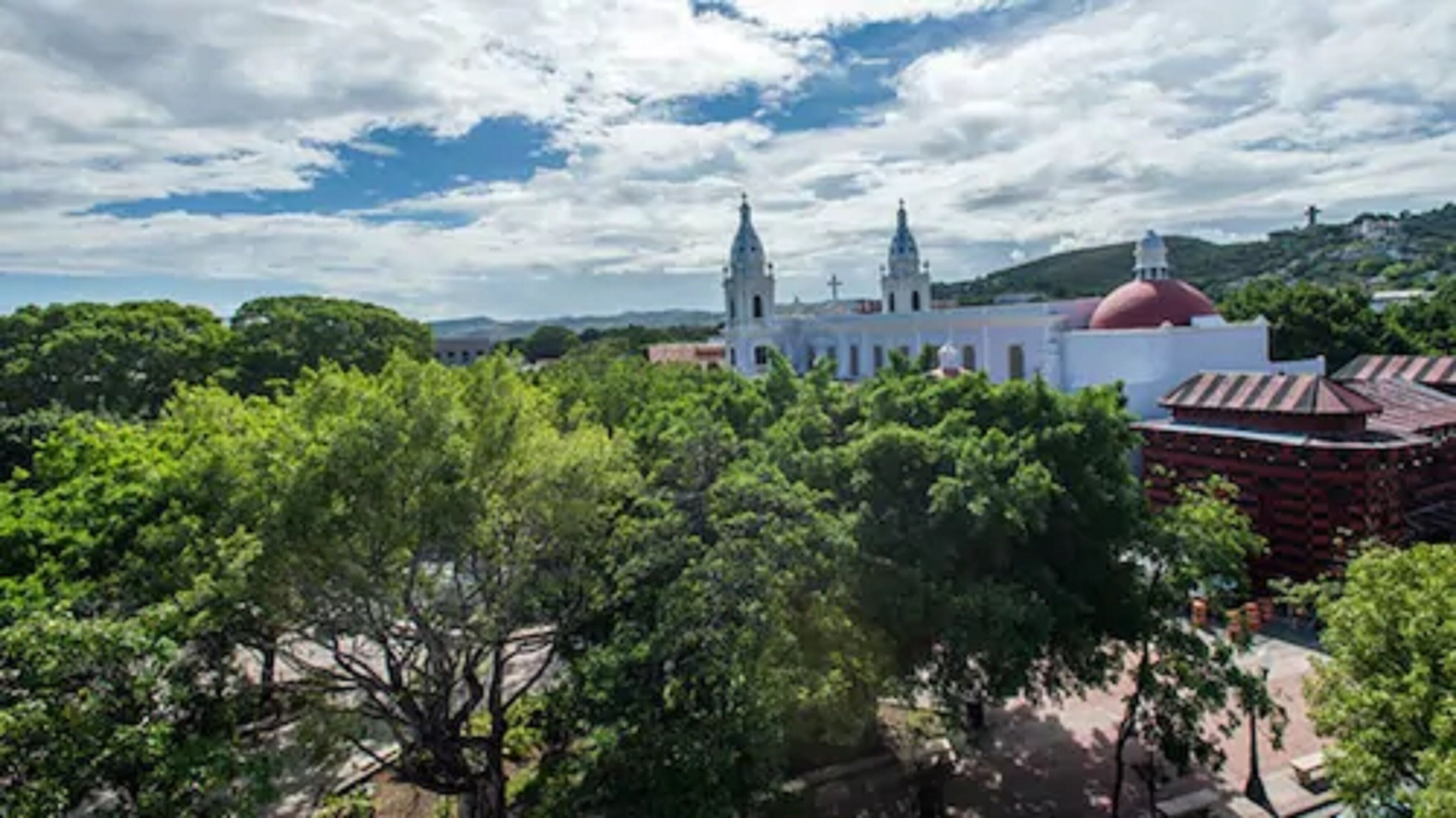 A historic building with two prominent towers and a red dome, surrounded by lush green trees.