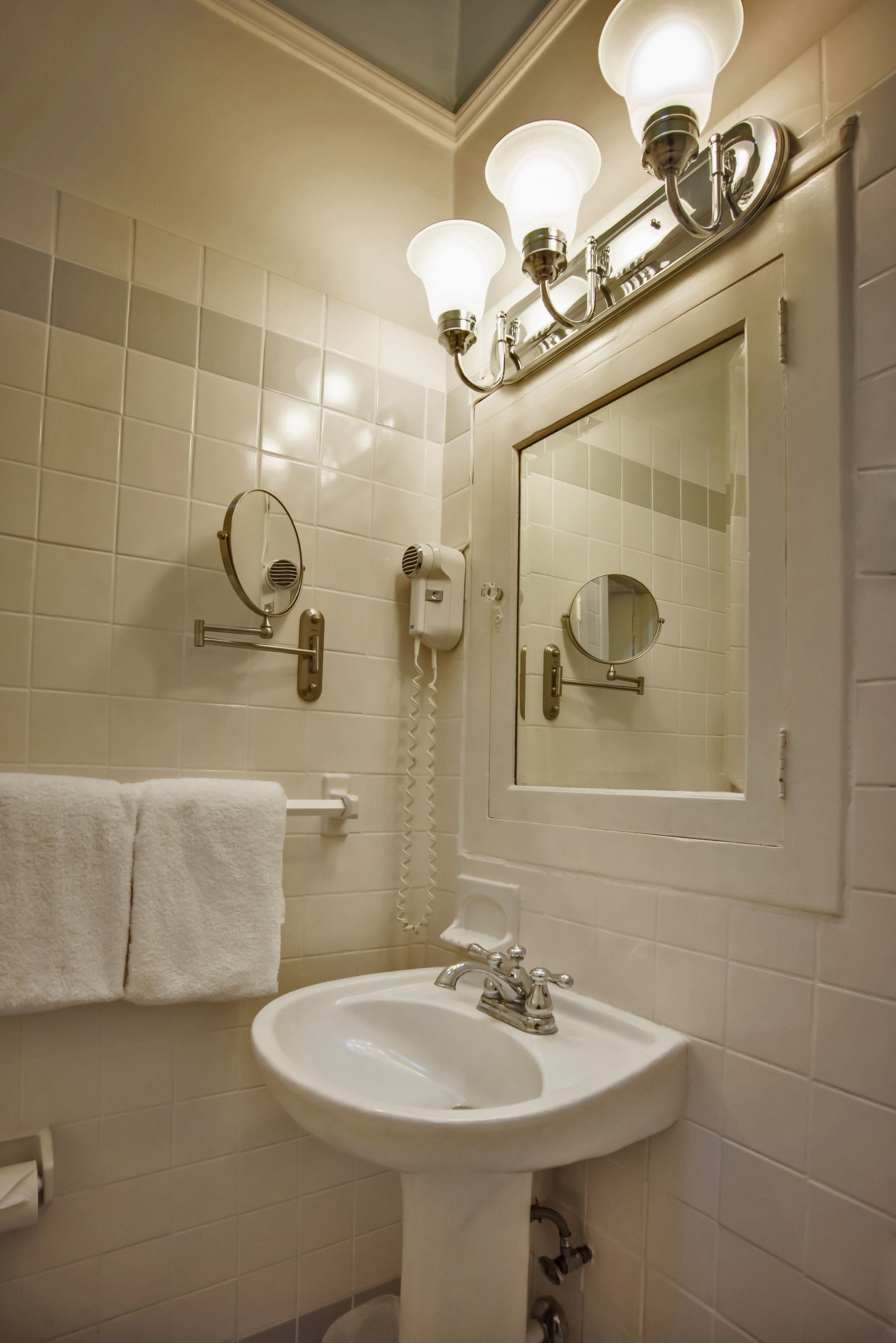 A bathroom with a sink, mirror, towel rack, and wall-mounted hairdryer.