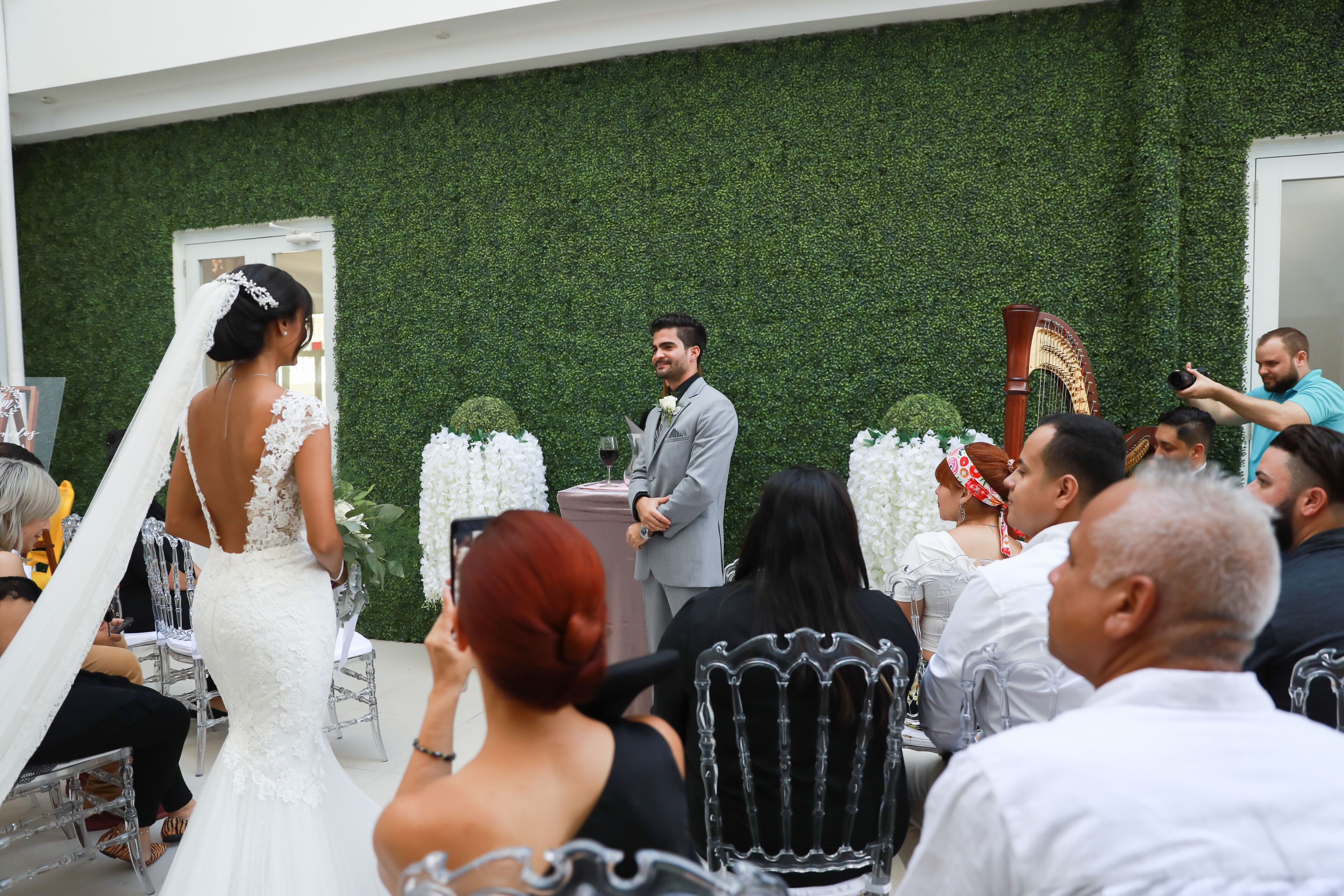 A wedding ceremony with guests seated in rows, a bride in a white dress, and a groom in a grey suit.