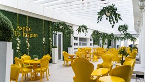 A spacious indoor area with yellow chairs and tables arranged in rows, a green wall with hanging plants, and a white ceiling with hanging lights. - Meliá Century Hotel Ponce (Ponce)