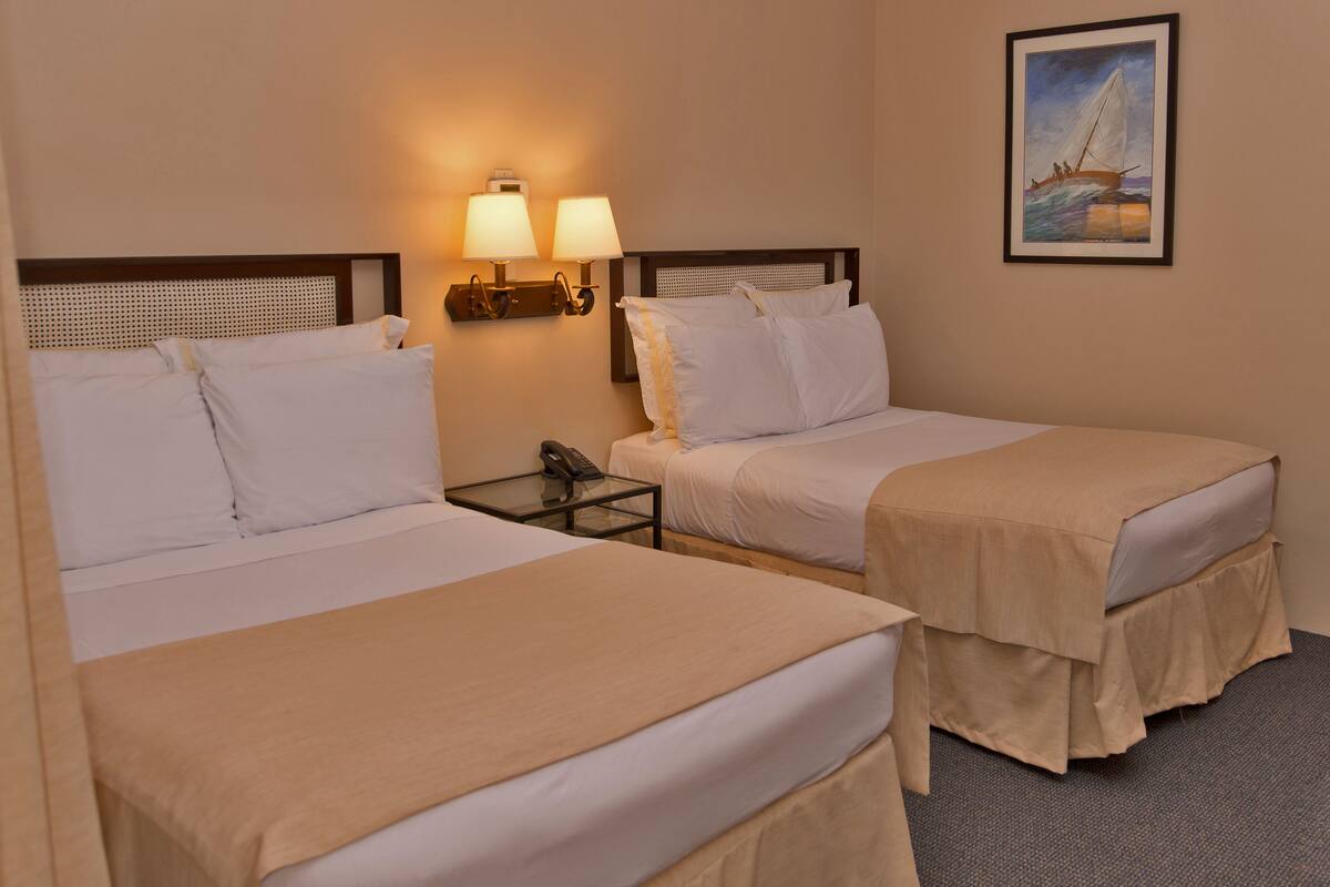 A hotel room with two beds, a nightstand with a phone, and a painting on the wall.