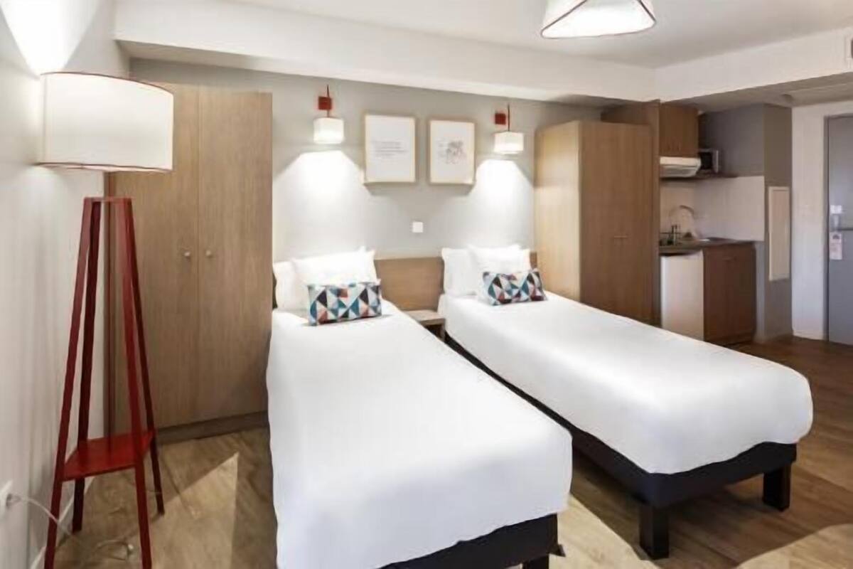 A hotel room with two beds, a desk, and a kitchenette.