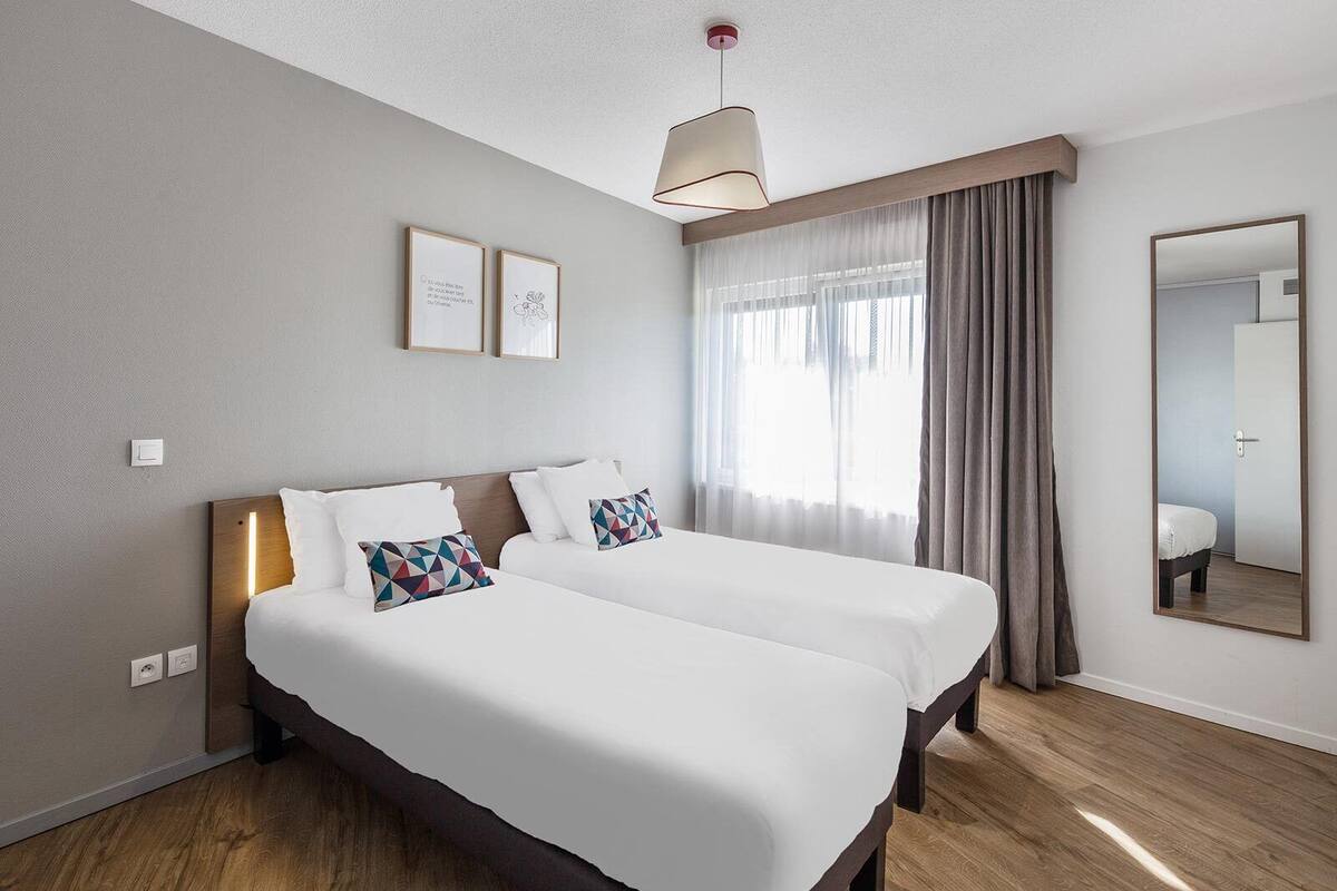 A hotel room with two beds, a large mirror, and a window with curtains.