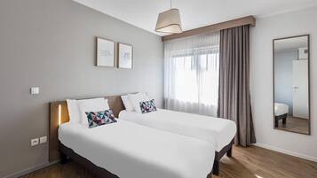 Una habitación de hotel con dos camas, un espejo grande y un ventanal con cortinas.