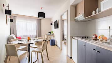 A modern kitchen with a built-in stove, a sink, and cabinets. There is a dining area with a round table and chairs, and a window with curtains.