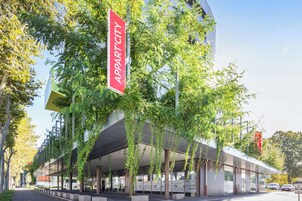 Un edificio moderno con un llamativo letrero rojo que dice 'APPARTCITY' y una zona de entrada cubierta.
