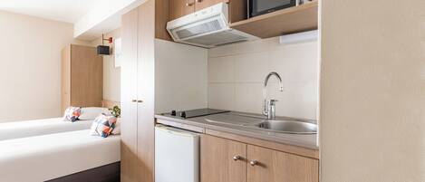 A compact kitchenette with a microwave, stove, sink, and a small refrigerator.