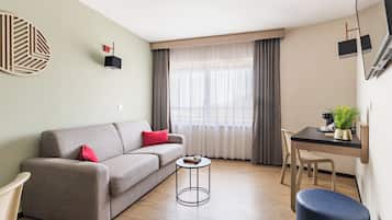 A modern living room with a sofa, a small round table, a dining area with a chair, and a large window with curtains.
