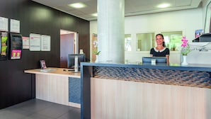 A reception desk with a modern design, including a large pillar, a computer, and a vase with flowers. - Appart'City Confort Mulhouse (Mulhouse)