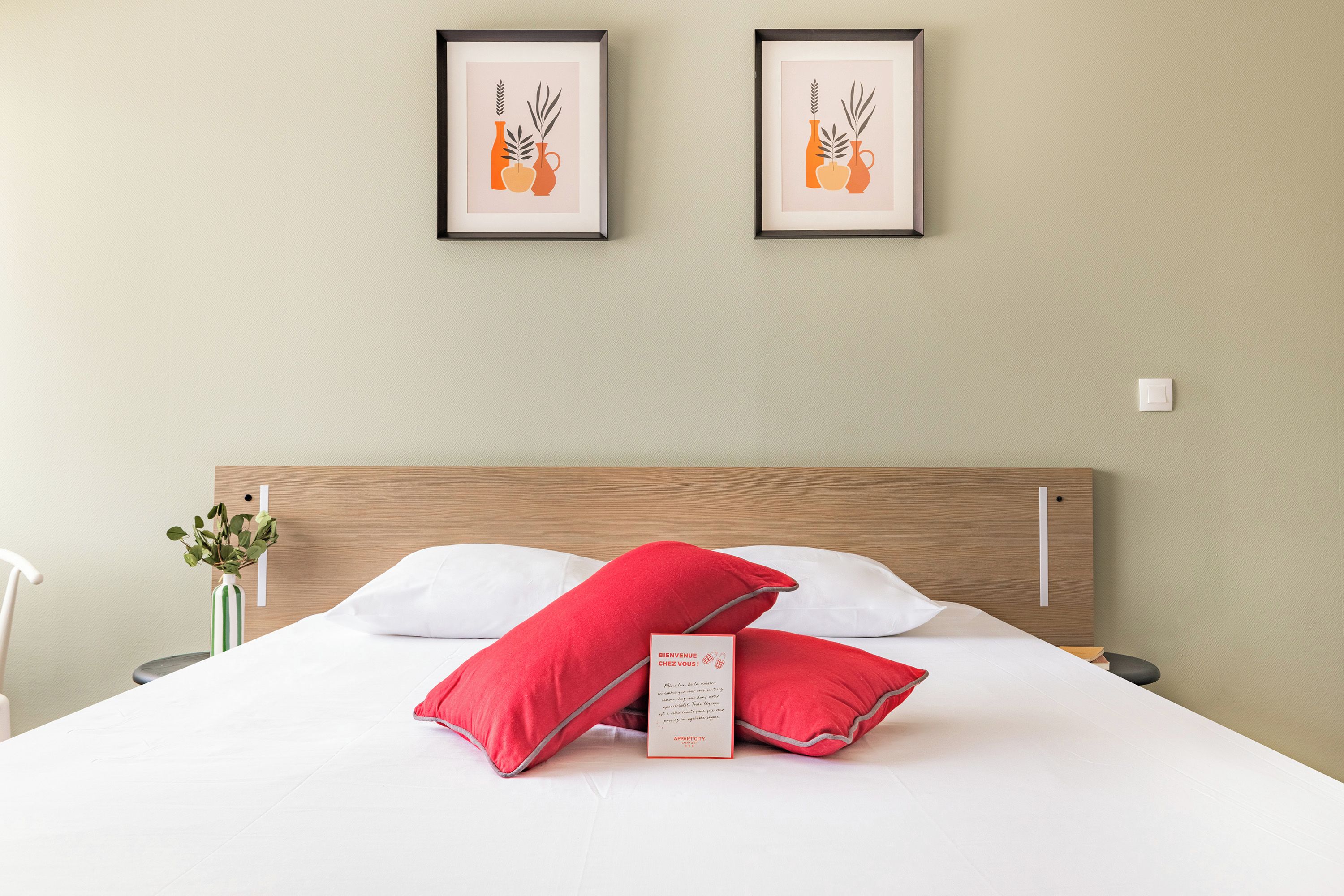 Ein Hotelzimmer mit einem hölzernen Kopfteil, weißer Bettwäsche und zwei gerahmten Kunstwerken über dem Bett.