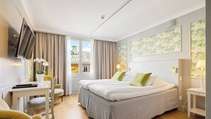 A hotel room with a bed, a desk, a chair, a TV, and a window with curtains.