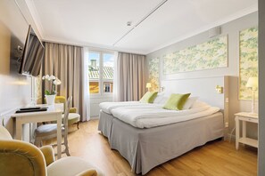 A hotel room with a bed, a desk, a chair, a TV, and a window with curtains.