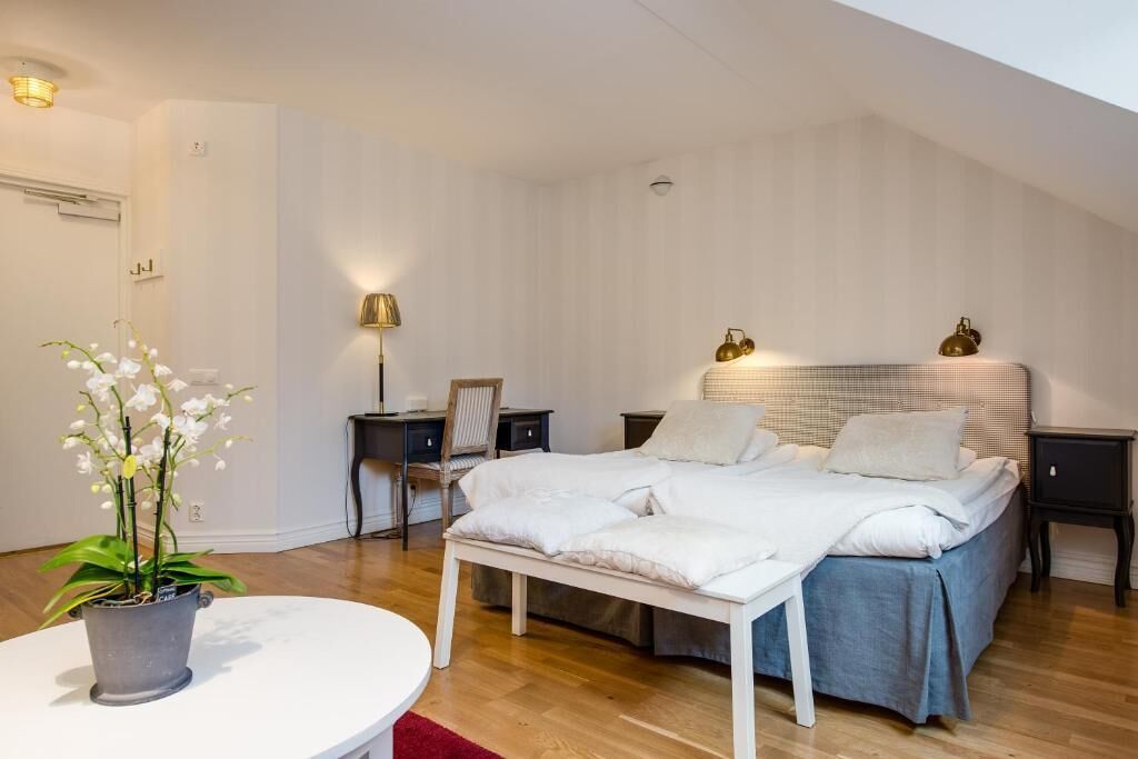 A bedroom with a bed, bedside tables, a desk, a chair, a potted plant, and a small table.