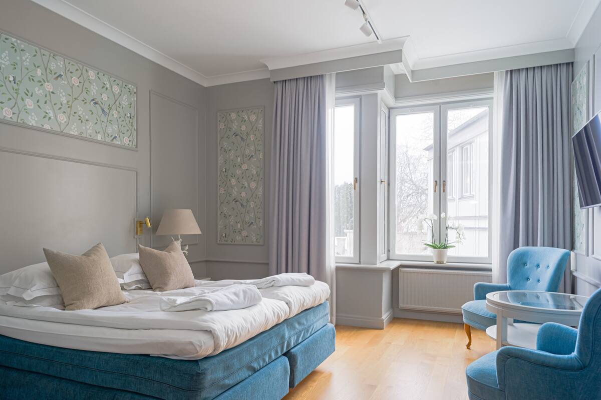 A bedroom with a bed, a chair, a window, and a TV.