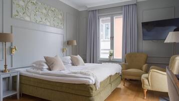 Quarto de hotel com cama, duas mesas de cabeceira, uma cadeira, televisão e janela com cortinas.