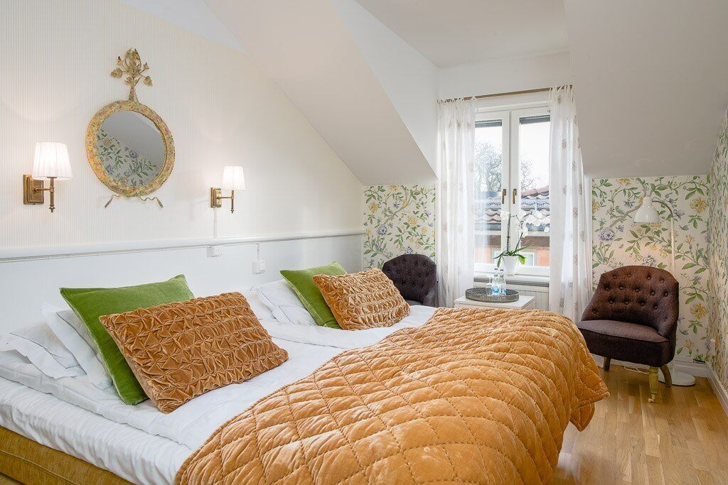 A bedroom with a bed, two wall sconces, a mirror, a window with curtains, and a chair.