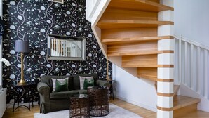 A staircase with wooden steps and white railings, a black floral wallpaper, a green sofa with cushions, and a white rug.