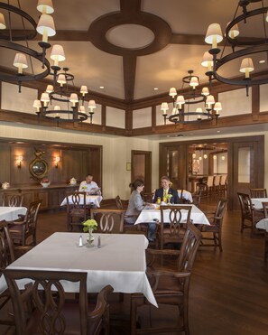 A restaurant with multiple tables and chairs, a chandelier, and a bar area.