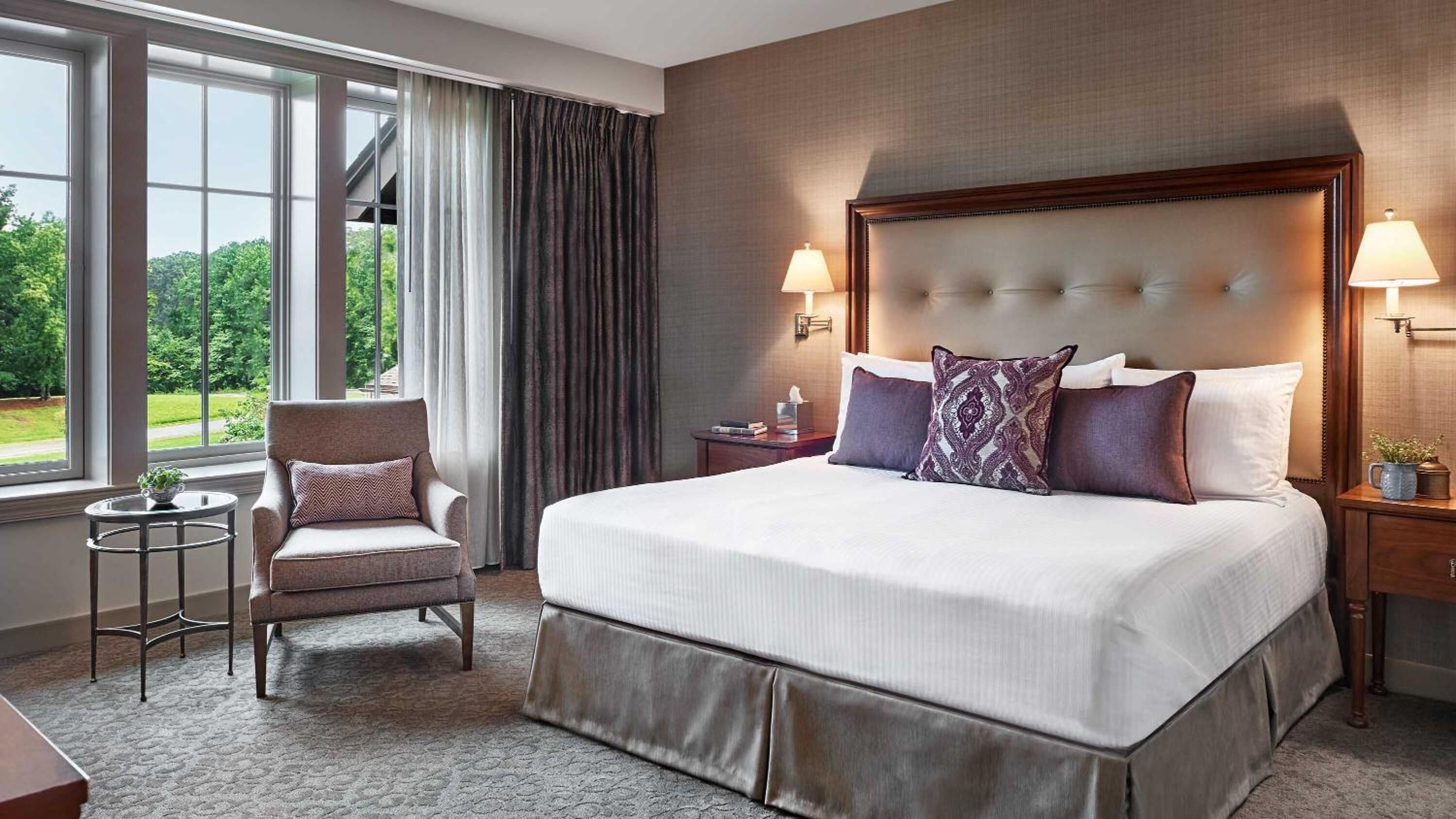 Una habitación de hotel con una cama grande, una silla, una mesita de noche y una ventana con cortinas.