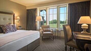 Ein Hotelzimmer mit einem großen Bett, zwei Sesseln, einem kleinen Tisch und Blick auf einen Golfplatz durch die Fenster.