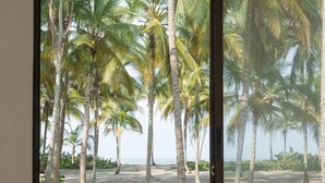 A room with a large sliding glass door leading to a beach with palm trees. - Tayrona Tented Lodge (Santa Marta)